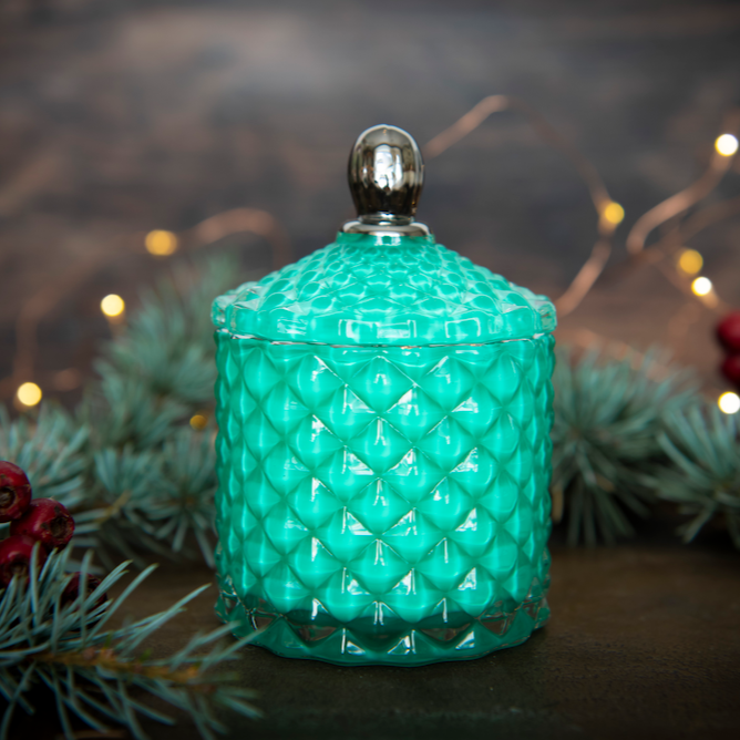 green glass jar candle with silver handle in alpine background