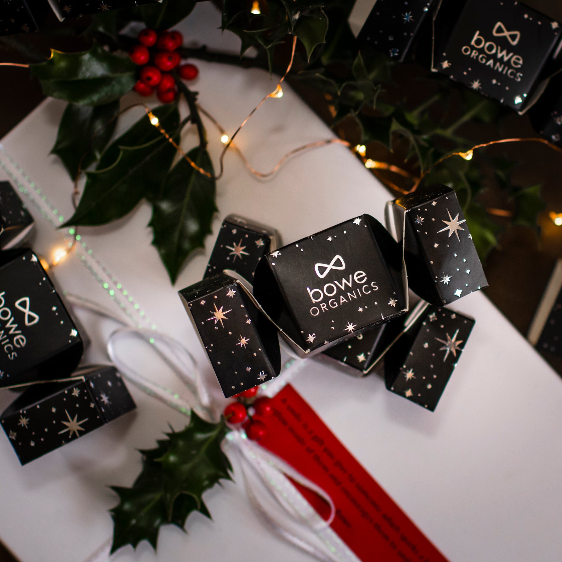 Bowe Organics Christmas Cracker. Vegan stocking stuffer. The cracker is placed amongst other crackers, another present in a white box and spirgs of holly.