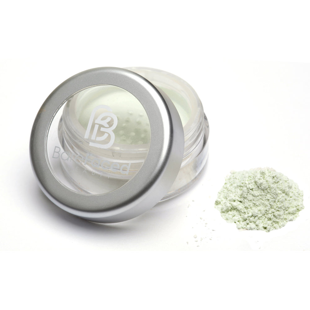 A small round pot of mineral colour corrector, with a swatch of the powder next to it showing a light green powder.