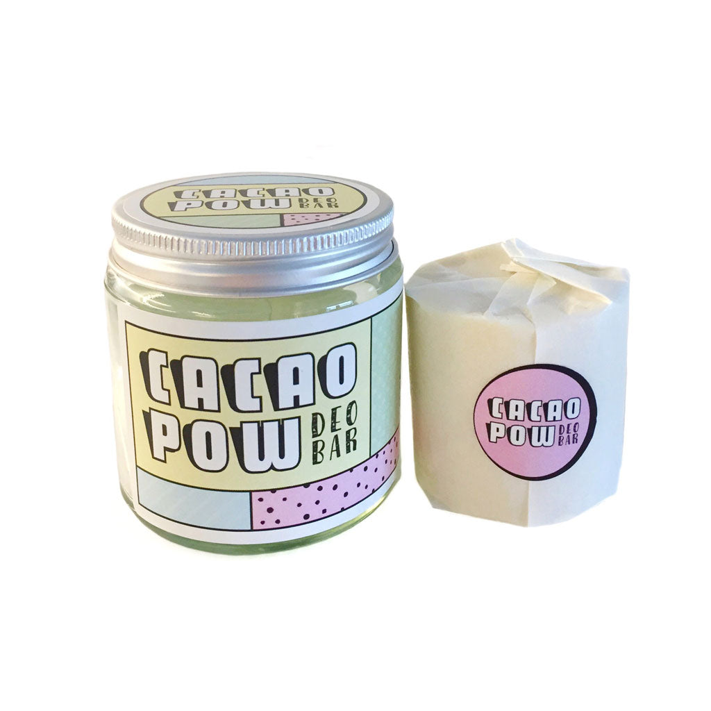 Photo of Cacao Pow natural deodorant bar in glass jar with aluminium lid and colourful label displaying product name. Next to the jar is the deodorant itself, wrapped in paper, sealed with a pink sticker of the product name. 