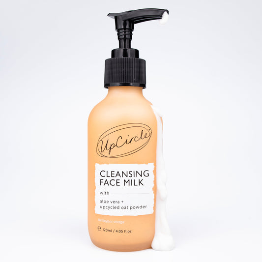 upcircle beauty's cleansing face milk with aloe vera and upcycled oat powder in an orange glass bottle with black plastic pump and white creamy cleanser running down the side on a white background