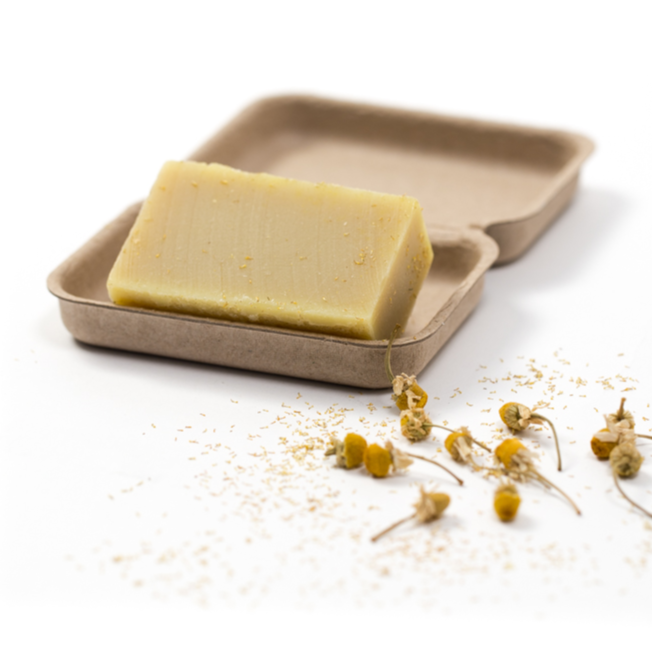 yellowy creamy coloured chamomile soap bar sitting in a brown kraft box surrounded by dry chamomile flowers