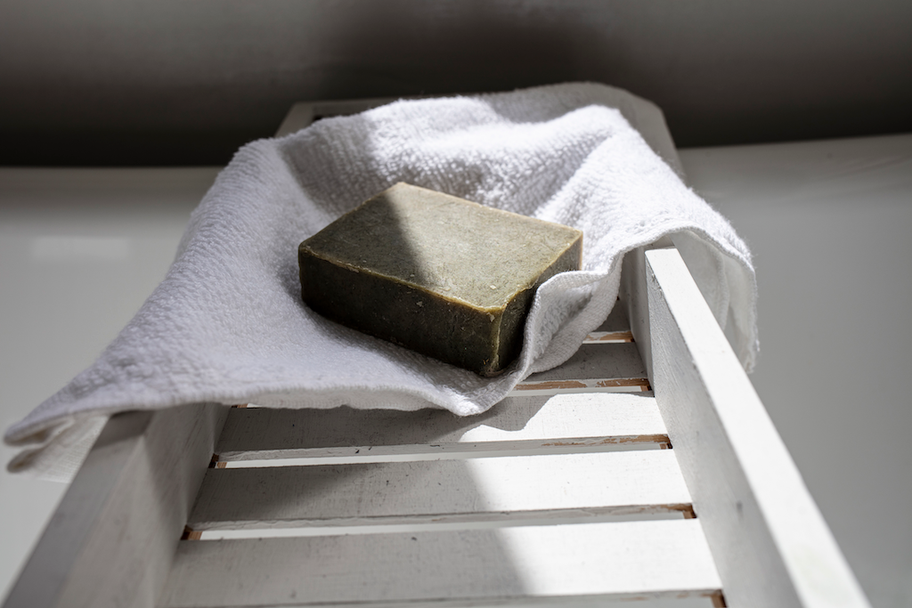 The nettle settle bar of soap is placed on top of a white towel, which has been placed on a white bath shelf.