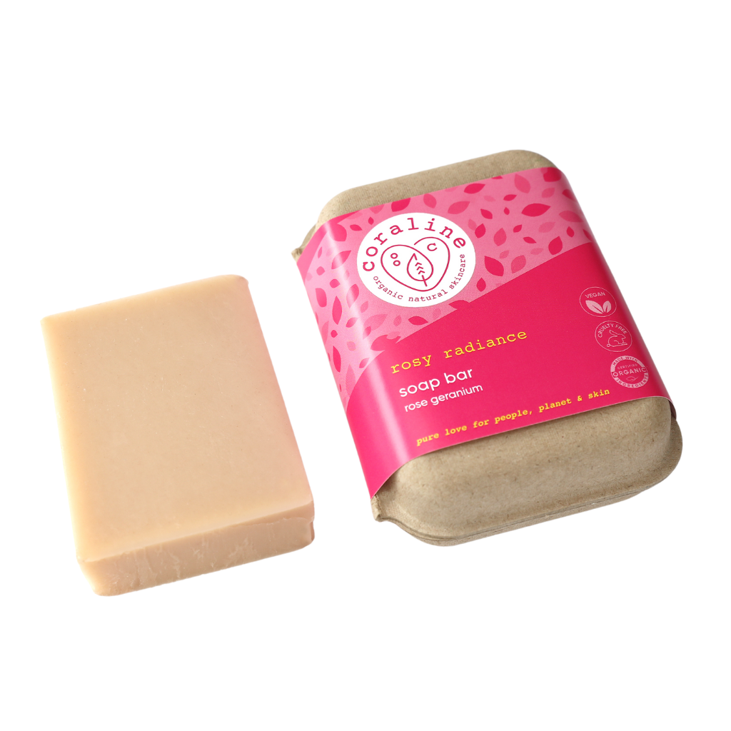 Coraline Skincare Rosy Radiance Soap Bar. Natural bar soap. The pink bar of soap is sitting next to the paper box it comes in with a bright pink paper sleeve.