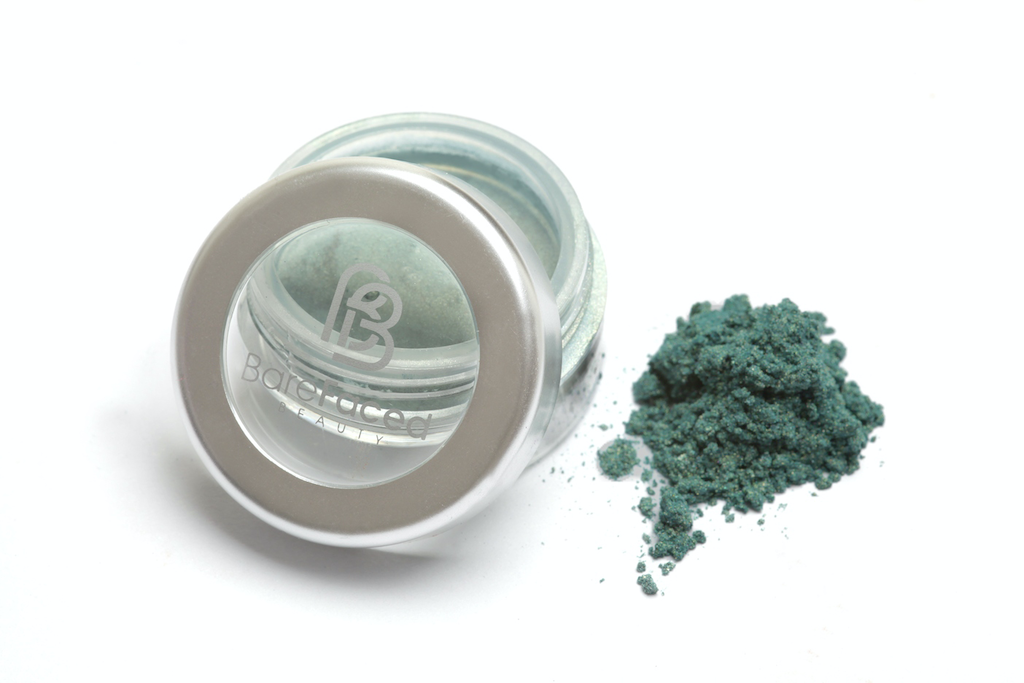 A small round pot of mineral eyeshadow, with a swatch of the powder next to it showing a matt pine green