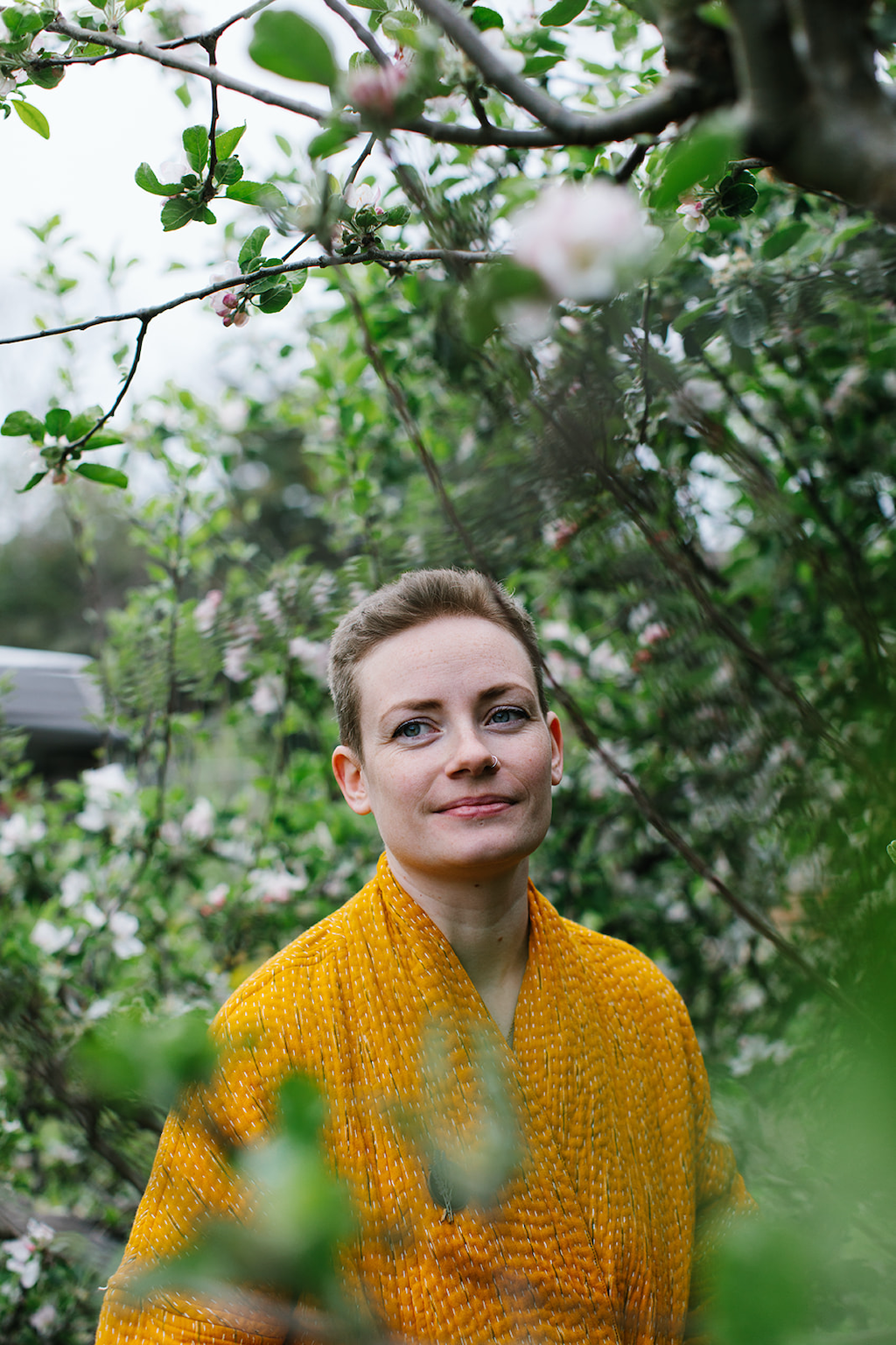 Forage Botanicals Founder Natasha. She is wearing a golden yellow robe and standing in the midst of a blooming floral tree.