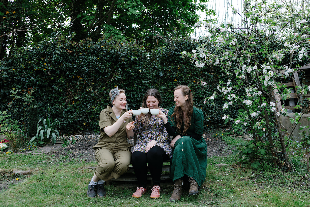 Forage Botanicals Rested Resilience Chai Latte Powder. Natural supplement for anxiety. Forage founder Natasha is sitting on the left with two other people enjoying a cuppa. They are sitting in a flourishing garden on a bench.
