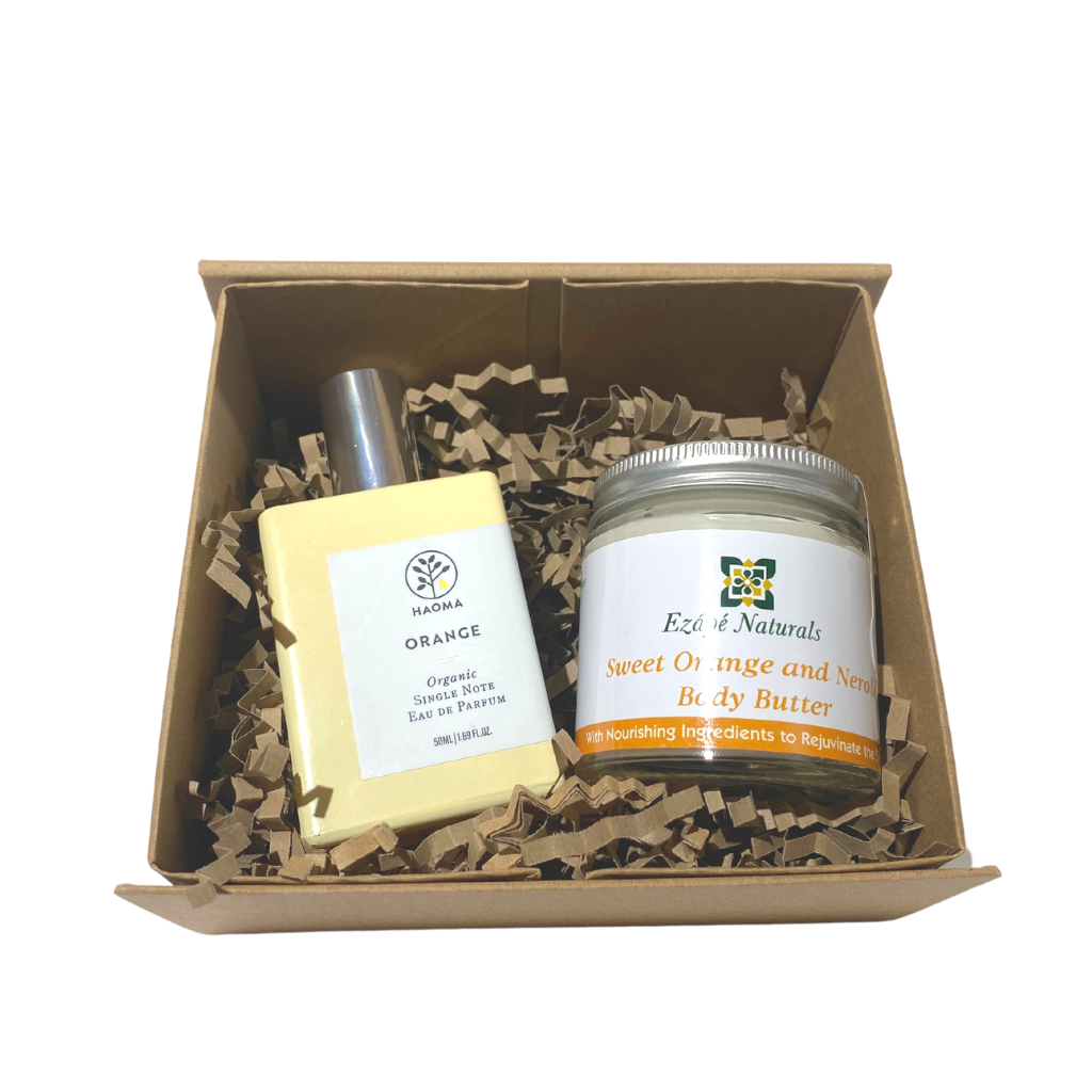 brown kraft cardboard gift box in a rectangular shape filled with brown kraft paper shred. the box has a flip over lid and magnetic fastening. inside the box you can see an organic perfume in a yellow bottle and a sweet orange and neroli body butter in a glass jar with an aluminium lid