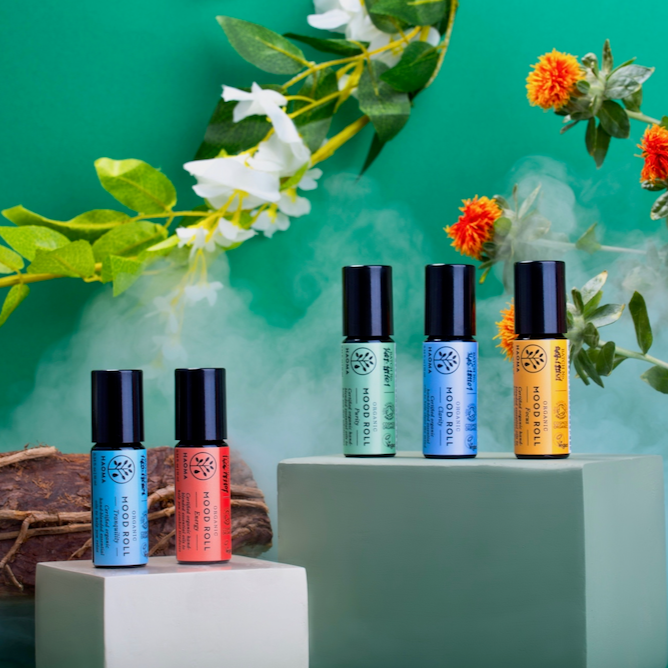 Haoma Aromatherapy Mood Rollers. Best aromatherapy mood lifters. The five mood rollers are pictured on green plinths with a green background and various plants behind.