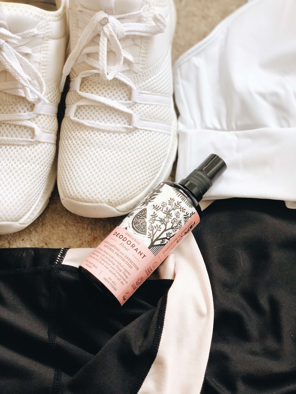 Haoma Organic Spray Deodorant. Natural spray deodorant. The Floral deodorant is sitting on some gym clothes with white trainers next to it.