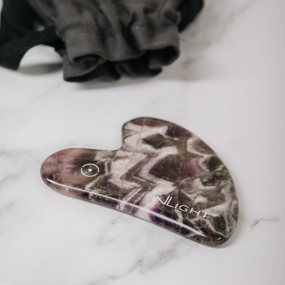 gua sha on marble surface with grey pouch in background