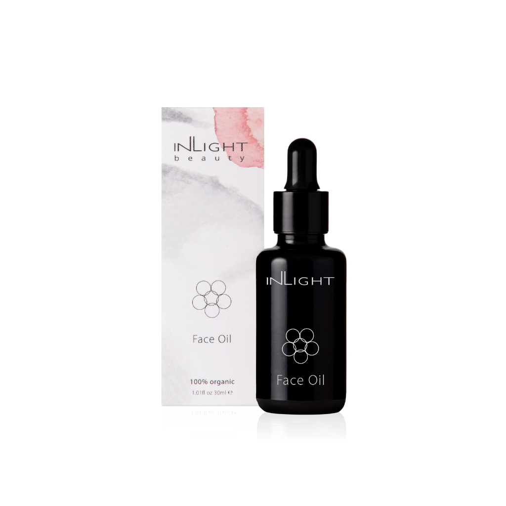 inlight beauty 100% organic face oil can be seen in it's black glass pipette bottle next to the cardboard box with white, grey and blush pink splashes on it on a white background