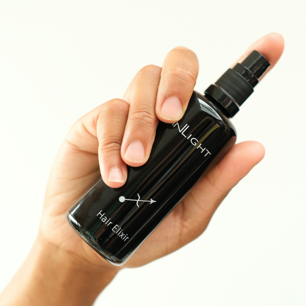 image of a hand holding a bottle of inlight beauty hair elixir with one finger on the pump as if they are about to dispense the organic hair oil.