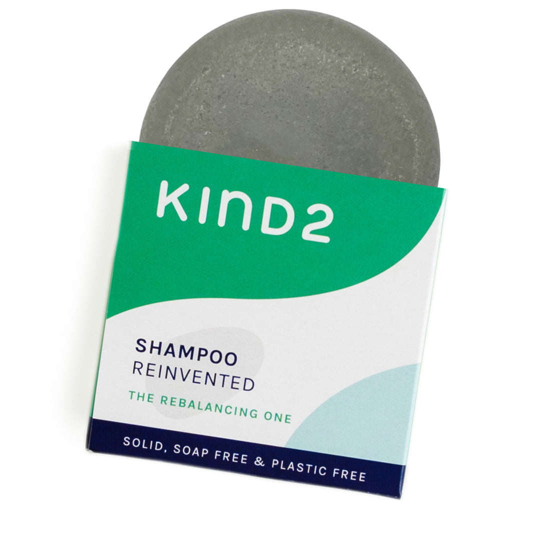 An image of the white/green cardboard box of the KIND2 rebalancing shampoo bar with a partial view of the bar in it