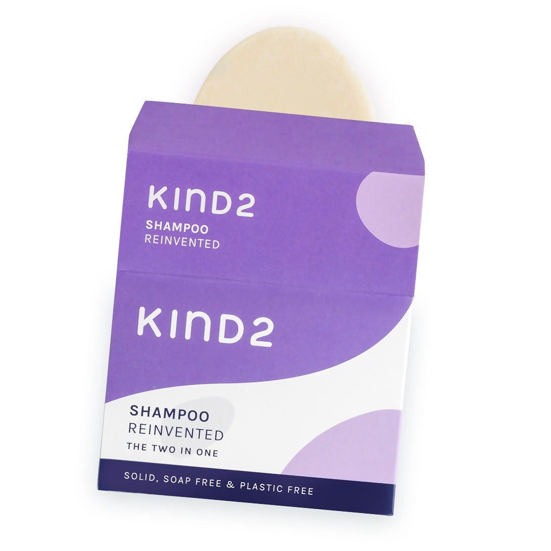 An image of the white and purple cardboard box of the KIND2 two in one shampoo bar with a partial view of the bar in it