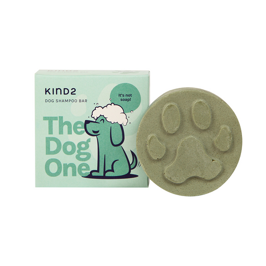 Round olive coloured soap bar, stamped with a paw print, advertising KIND2 Neem & Lavender natural dog shampoo. Placed in front of the light green square box it comes in, with a happy soaped up dog illustration.
