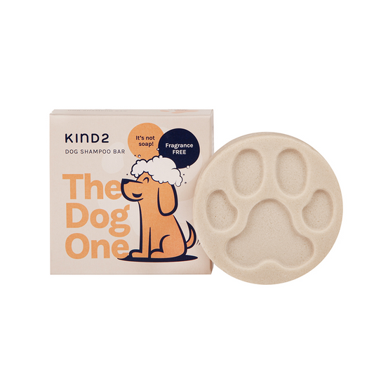 Round cream coloured soap bar, stamped with a paw print, advertising KIND2 Fragrance free natural dog shampoo. Placed in front of the light orange square box it comes in, with a happy soaped up dog illustration.