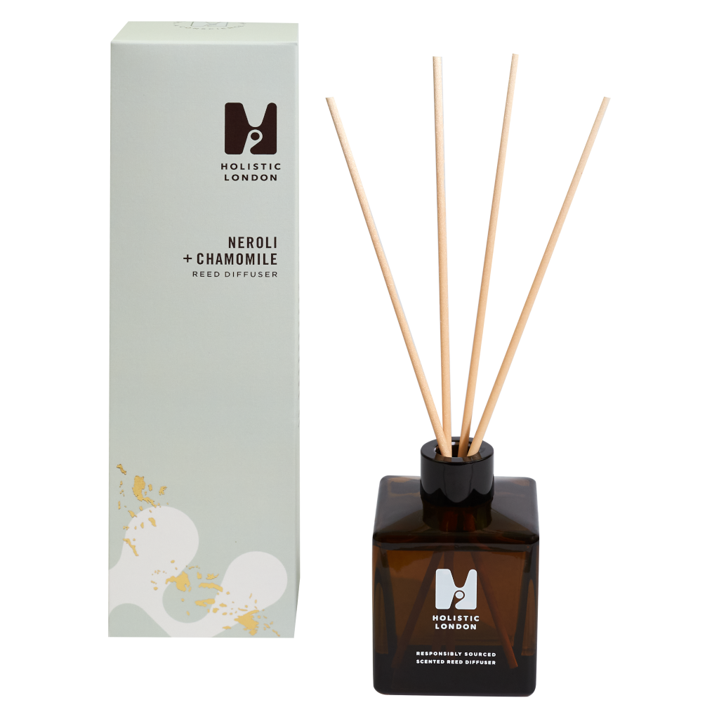 photograph of holistic london's neroli + chamomile reed diffuser on a white background. on the left side of the image is the light green cardboard box with the holistic london logo on it. the label reads ' neroli + chamomile reed diffuser’. on the right side of the photo is the amber glass bottle with 4 wooden reeds inside. the glass is printed with the holistic london logo and says 'responsibly sourced scented reed diffuser’