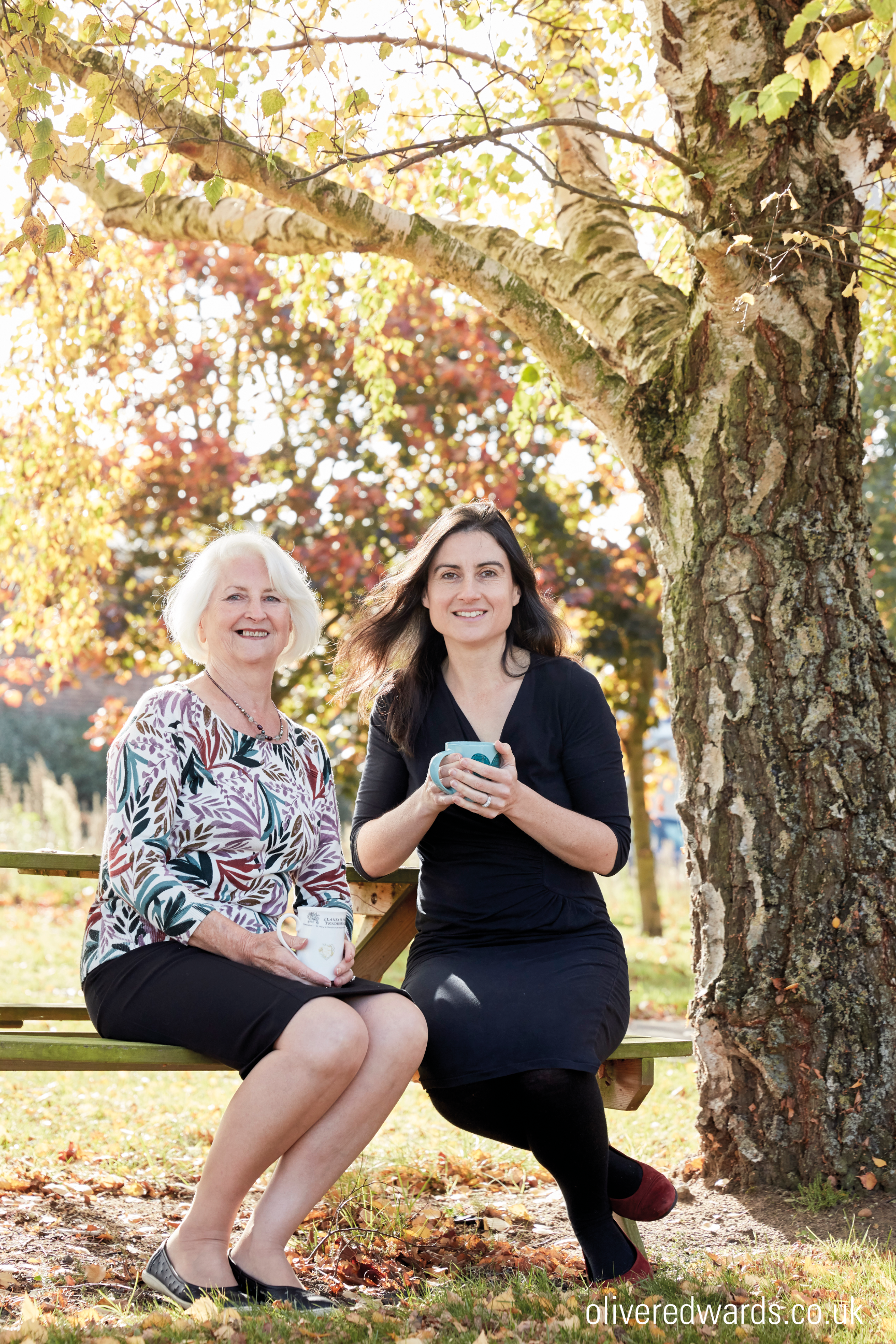 Odylique founder Margaret with daughter Abbie, sitting on a bench under a tree.