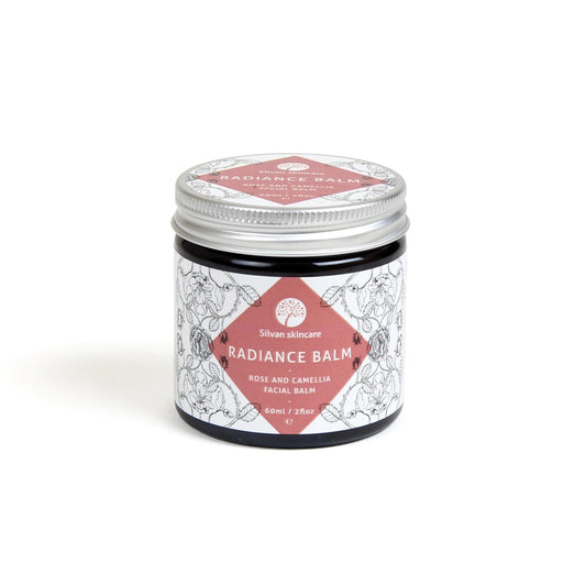 A glass jar of silvan skincare radiance balm. The small jar has an aluminium lid and the label is white with a pink diamond surrounded with botanical illustrations.
