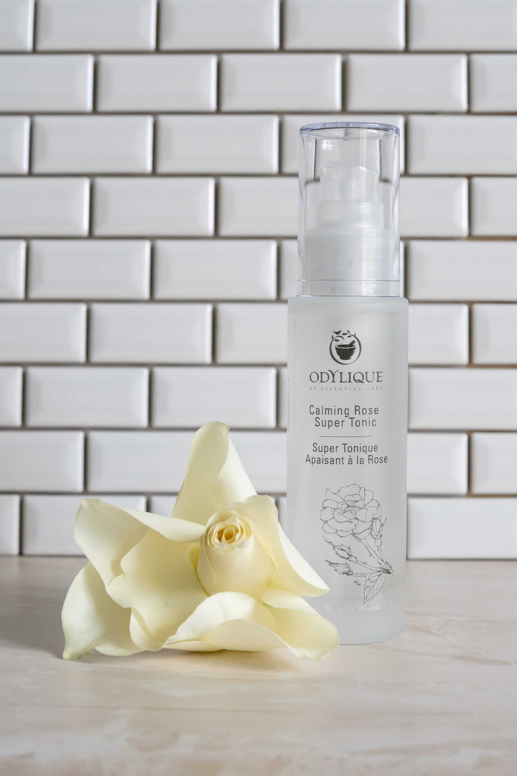 odylique rose toner with rose flower sitting on a counter top with white tiles and grey grouting behind it