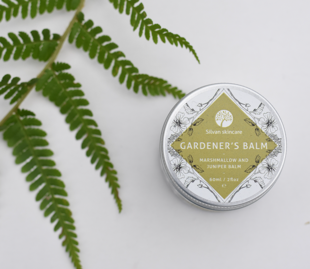 Silvan Skincare Gardener's Balm. Plastic free skincare. Pictured in an amber glass jar with an aluminium lid with a delicately illustrated white and olive green label from the top, with a fern next to it.