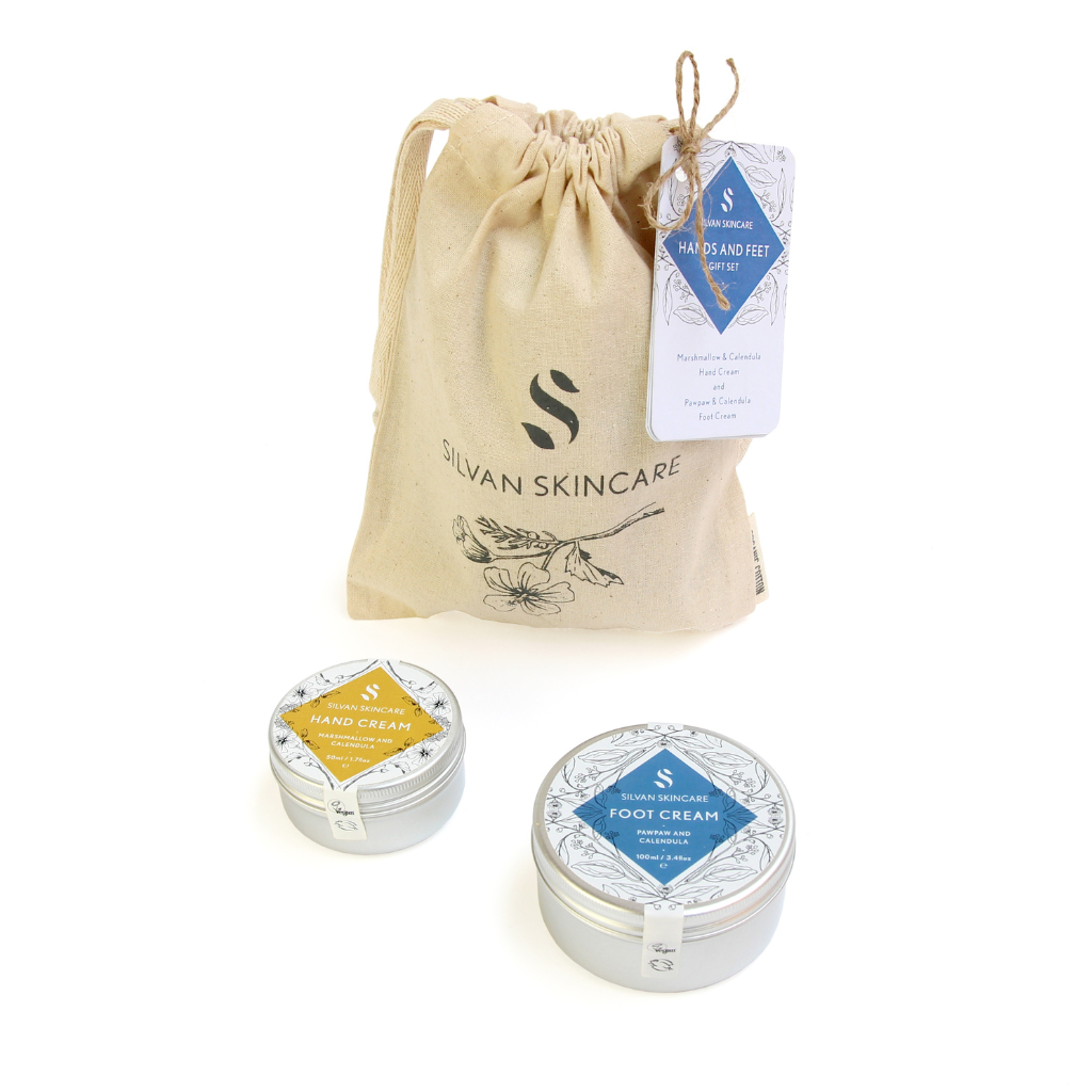 Silvan Skincare Hands and Feet Gift Set. Vegan gifts. The tin of hand cream with a yellow label and the slightly larger tin of foot cream with a blue label are sitting in front of the organic cotton drawstring gift bag with the Silvan logo on it.