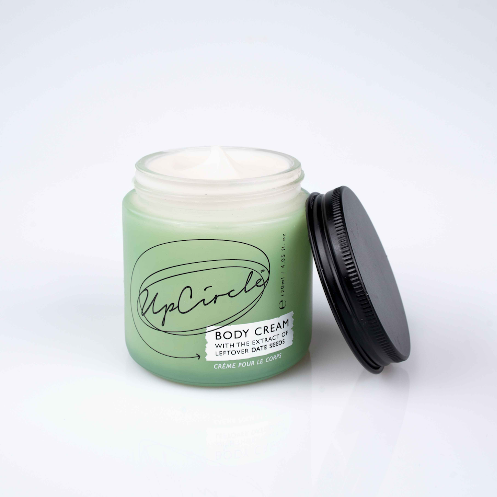 UpCircle Beauty Body Cream with Aloe Vera and Cocoa Butter. Natural body lotion. The green glass jar is sitting open with the black aluminium lid next to it, showing the white lotion inside.