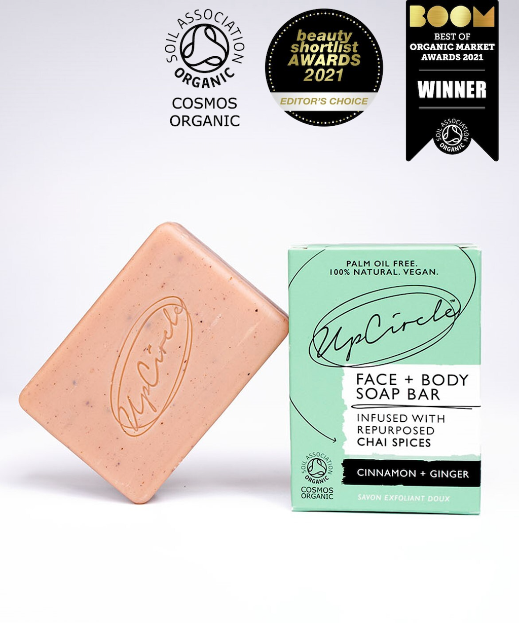 UpCircle Cleansing Soap Bar with Cinnamon and Ginger. Certified organic soap. The pink soap bar is leaning against its green branded box. A number of awards and certifications are overlaid on the image.
