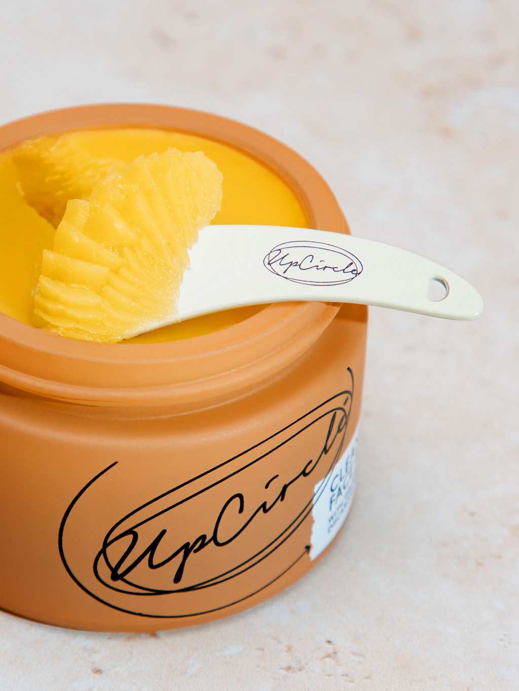 UpCircle Cleansing Face Balm. Sustainable skincare. The orange glass jar containing the balm is shown open from above, with a spatula and some scooped up product in it.