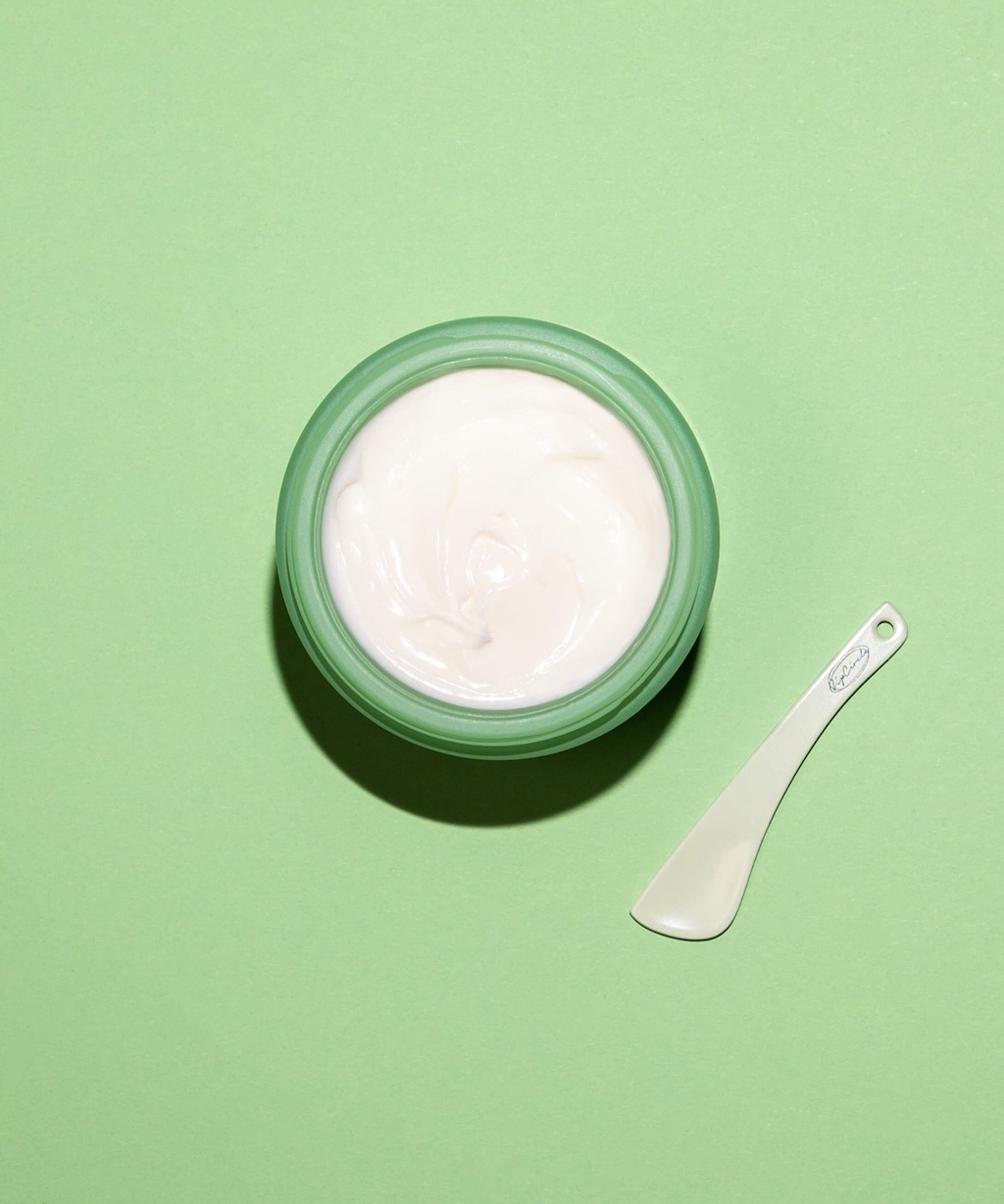Upcircle Cosmetic Spatulas. Recyclable beauty accessories. One of the spatulas is pictured on a green surface, next to an open green pot of white cream product.