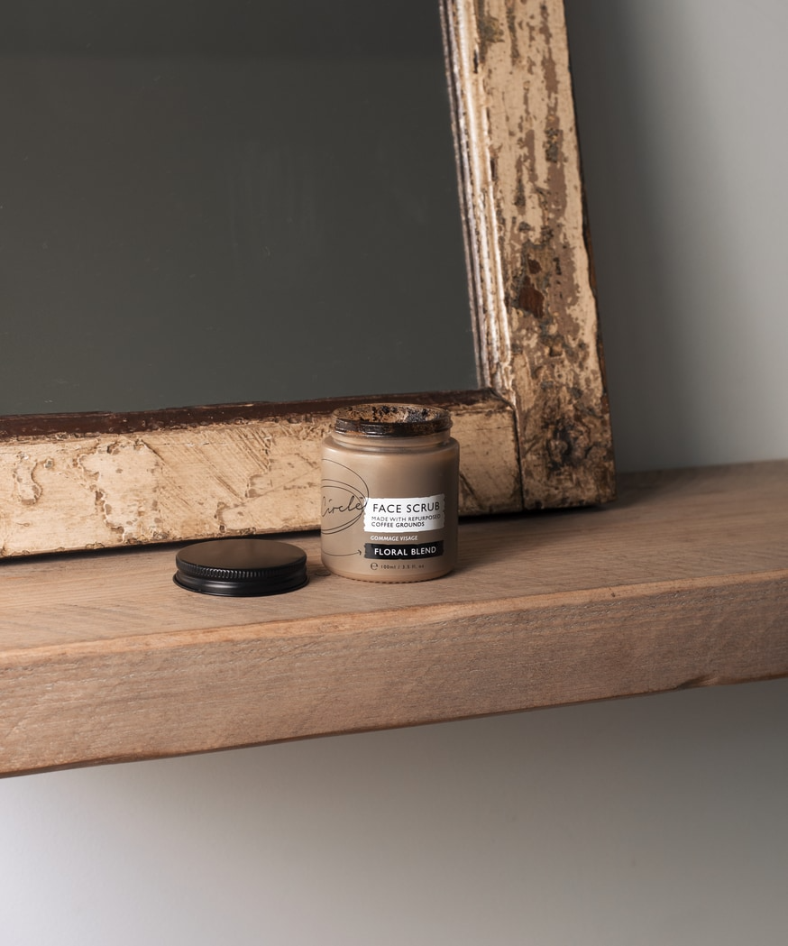 upcircle skincare's floral and coffee face scrub sitting on a chunky natural wooden ledge with a rustic mirror behind it