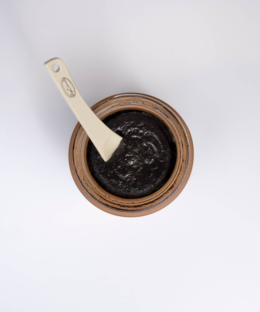 upcircle coffee face scrub aerial view with one of their reusable metal spatulas immersed in the scrub which is a rich chocolatey brown colour