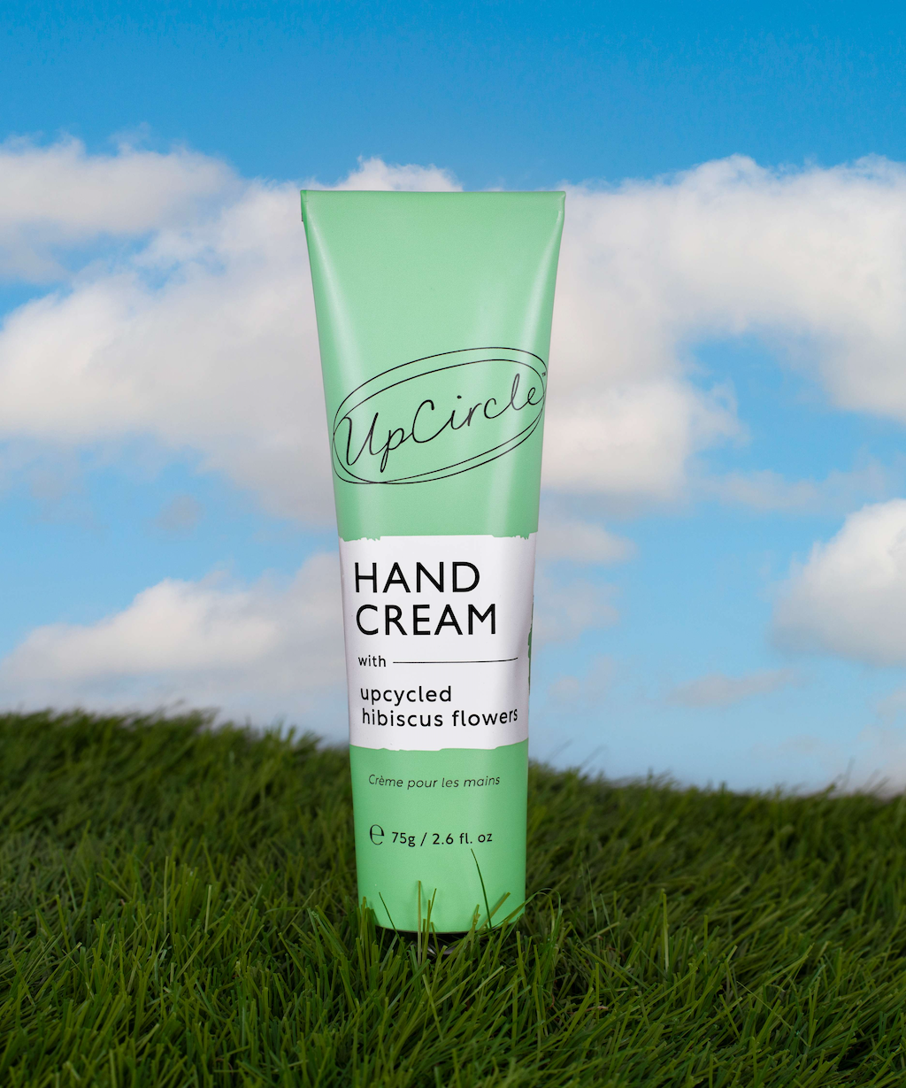 photo of the upcircle hand cream in a green tube with white label super imposed on a background with bright green grass and bright blue sky with white clouds 