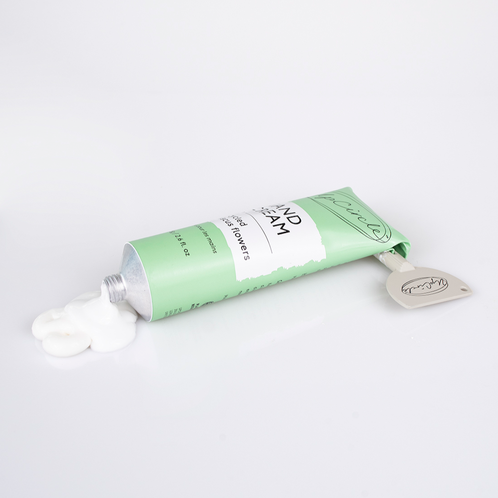 side view of the upcircle hibiscus hand cream which comes in a light green aluminium tube. you can see that the upcircle tube key squeezer has been used to roll down the aluminium tube in order to use every bit of cream and to dispense it. there is a large dollop of hand cream coming out of the tube 